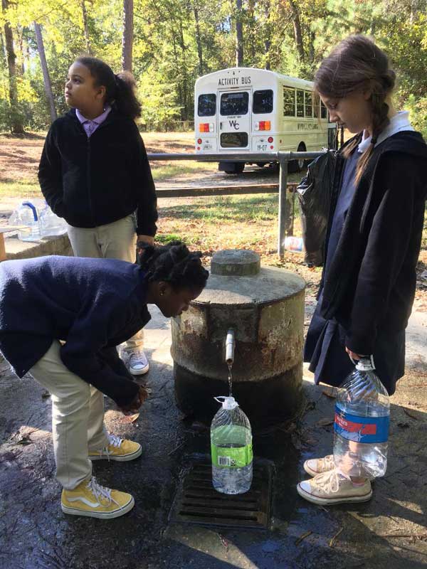 Three students observing the spring filling a water jug.