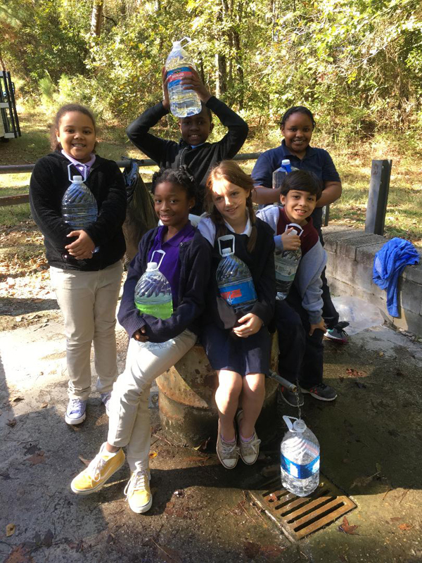 Six students with full water jugs at the spring.