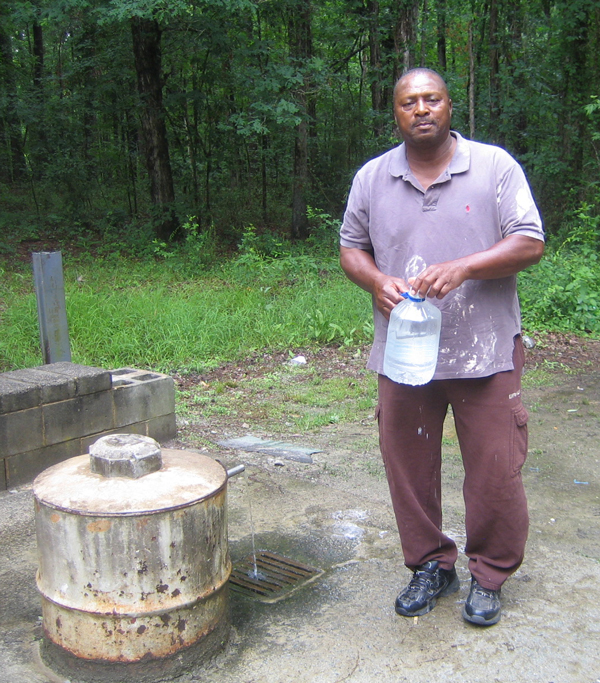A man stands next to the spring, carrying a jug filled with water.
